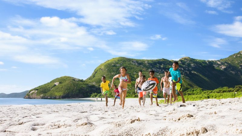 Children and adults playing rugby on a Fiji beach
