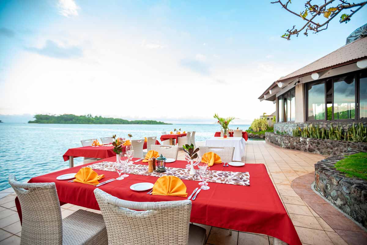 Outdoor dining tables beside the lagoon at Koro Sun Resort