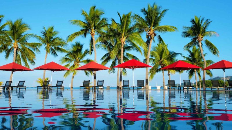 Palm trees and red umbrellas reflected in Musket Cove’s main resort pool