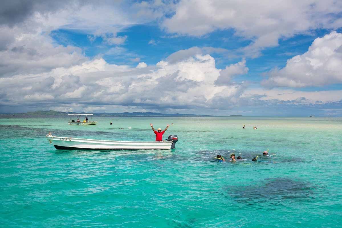 Guests snorkelling beside a small boat in the clear waters near Musket Cove