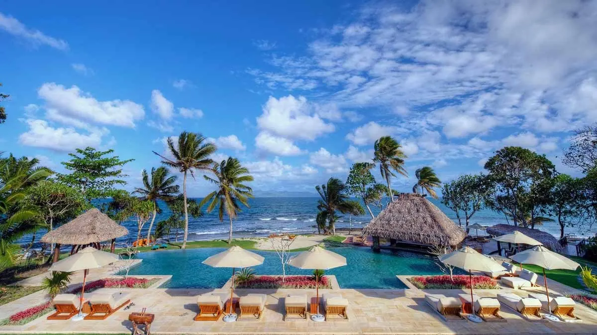 Main swimming pool framed by palms and thatched roofs at Nanuku Resort Fiji