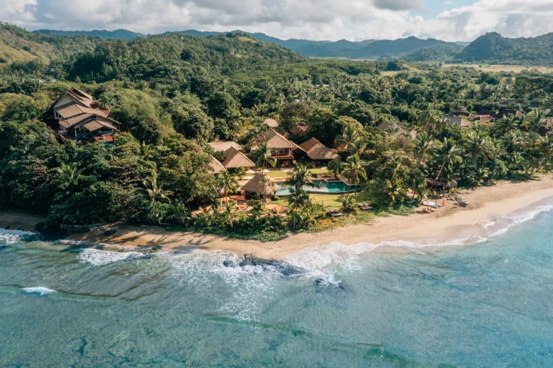 Aerial view of Nanuku Resort Fiji with its beachfront, main pool and lush green hills