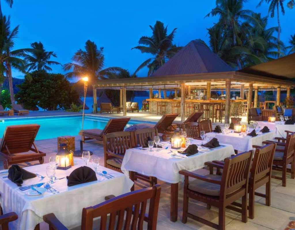 Outdoor tables set for evening dining beside the pool at Paradise Cove Resort