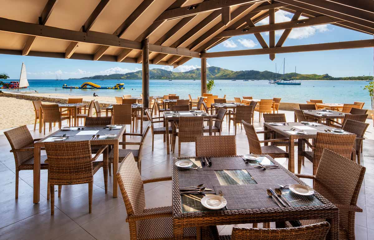 Open-air dining tables overlooking the beach and lagoon at Plantation Island Resort