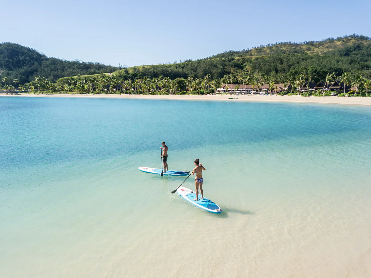 Guests stand-up paddleboarding in the bay at Six Senses Fiji