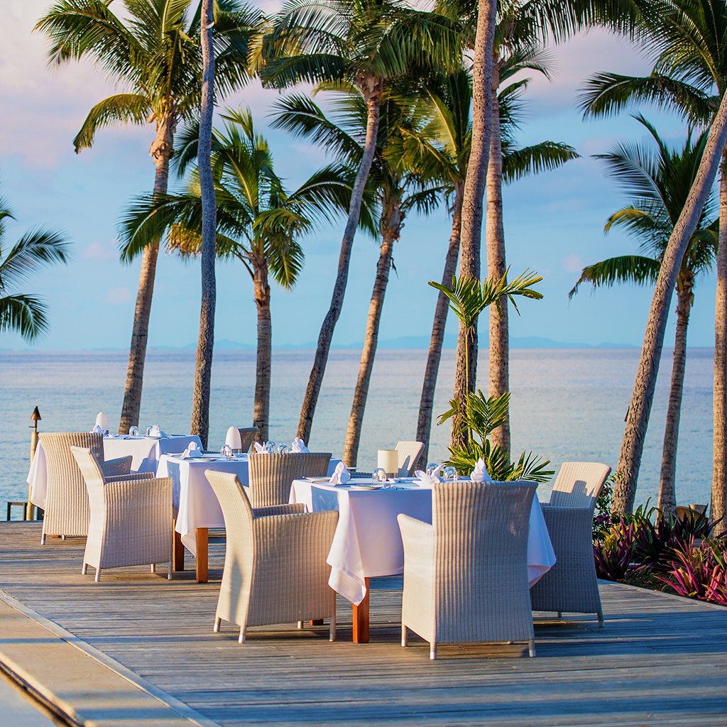 Dining tables beneath palms beside the beach at VOMO Island Resort